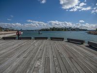 two wooden benches overlook the water of a body of water with boats in it and people walking along it