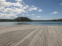 the wooden pier sits under a partly cloudy blue sky above the water with small island in the distance