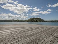 the wooden pier sits under a partly cloudy blue sky above the water with small island in the distance