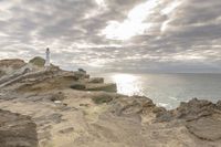 a rocky cliff overlooks the ocean with a lighthouse at the top of the cliff