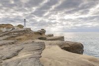 a rocky cliff overlooks the ocean with a lighthouse at the top of the cliff