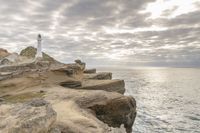 a rocky cliff overlooks the ocean with a lighthouse at the top of the cliff