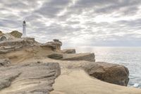 a rocky cliff overlooks the ocean with a lighthouse at the top of the cliff