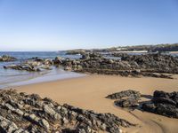 a body of water surrounded by rocks near a sandy beach by a rocky shore line