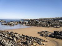 a body of water surrounded by rocks near a sandy beach by a rocky shore line