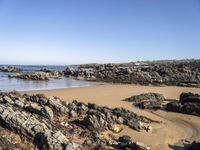 a body of water surrounded by rocks near a sandy beach by a rocky shore line