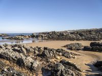 a body of water surrounded by rocks near a sandy beach by a rocky shore line