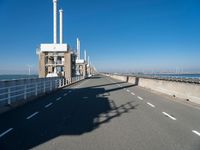 an empty road runs underneath a large power station structure with tall towers in the background