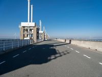 an empty road runs underneath a large power station structure with tall towers in the background