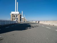 an empty road runs underneath a large power station structure with tall towers in the background