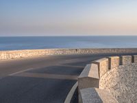 a very wide empty highway with some big rock walls in front of the ocean and sky