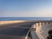 a very wide empty highway with some big rock walls in front of the ocean and sky