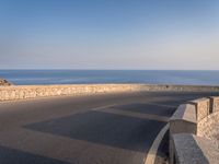 a very wide empty highway with some big rock walls in front of the ocean and sky