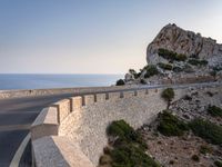 a very wide empty highway with some big rock walls in front of the ocean and sky