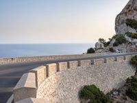 a very wide empty highway with some big rock walls in front of the ocean and sky