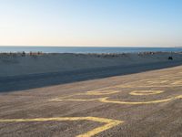 a street with a yellow line painted on it in the sand with an ocean in the background