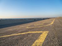 a street with a yellow line painted on it in the sand with an ocean in the background