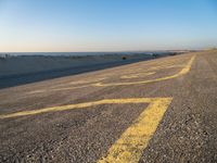 a street with a yellow line painted on it in the sand with an ocean in the background