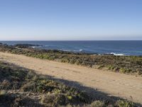 a road leading to the water and a body of water in the distance, with the beach just behind it