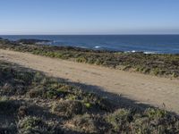 a road leading to the water and a body of water in the distance, with the beach just behind it