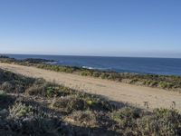 a road leading to the water and a body of water in the distance, with the beach just behind it