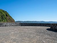 a view of the ocean from a sandy beach with a rock wall on it's edge