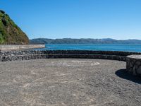 a view of the ocean from a sandy beach with a rock wall on it's edge