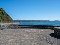 a view of the ocean from a sandy beach with a rock wall on it's edge