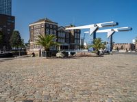 an empty bricked courtyard area by the water with water feature and buildings in the back ground