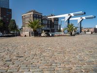 an empty bricked courtyard area by the water with water feature and buildings in the back ground