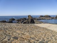 a sidewalk with stepping steps leading to the water on a rocky shore with clear blue sky in background