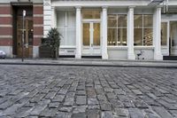 a paved cobblestone street and brick buildings in the city with people walking on the sidewalk