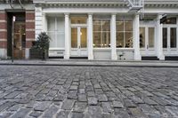 a paved cobblestone street and brick buildings in the city with people walking on the sidewalk