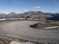 a circular concrete surface in the middle of the road with mountains in the background, on which a metal railing is placed and blue painted