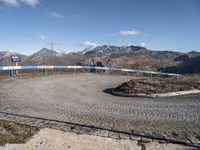 a circular concrete surface in the middle of the road with mountains in the background, on which a metal railing is placed and blue painted