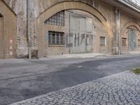 an empty street in front of a brick building with large arched windows and graffiti writing