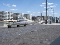 a city street with people walking and sitting by a bench with a boat docked in the background