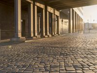 a street is shown with an old brick walkway in between two pillars and pillars, with sunlight shining on it
