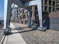 a paved walkway under a large metal structure, with a street light next to it