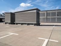 a row of benches next to a building with sky and clouds behind them in the parking lot