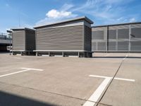 a row of benches next to a building with sky and clouds behind them in the parking lot