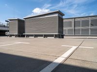 a row of benches next to a building with sky and clouds behind them in the parking lot