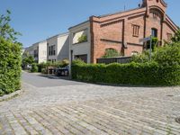 a brick paved parking lot with cars and buildings in the background and trees surrounding it