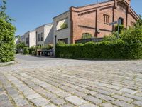 a brick paved parking lot with cars and buildings in the background and trees surrounding it