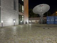 the satellite dish is illuminated in the courtyard of an old town building at night, in front of the garbage containers