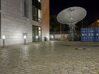 the satellite dish is illuminated in the courtyard of an old town building at night, in front of the garbage containers