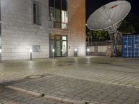 the satellite dish is illuminated in the courtyard of an old town building at night, in front of the garbage containers