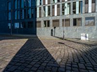 a shadow on a street next to a building with windows and a sign in the corner