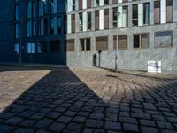 a shadow on a street next to a building with windows and a sign in the corner