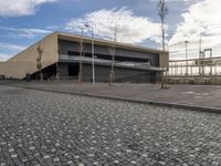 a long building on a side walk with brick in front of it and two people walking around the walkway